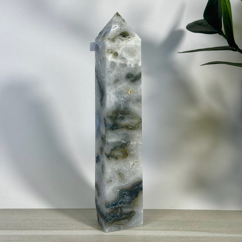 Tall, polished moss agate tower with white, grey, and dark green inclusions, standing on a light wooden surface.