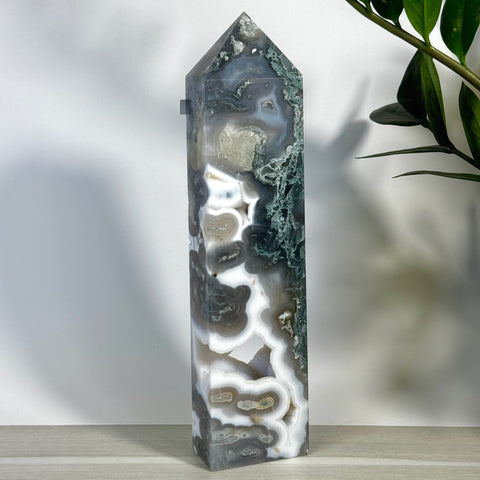 Tall, polished moss agate tower with white, gray, and green natural patterns, standing on a light wood surface.