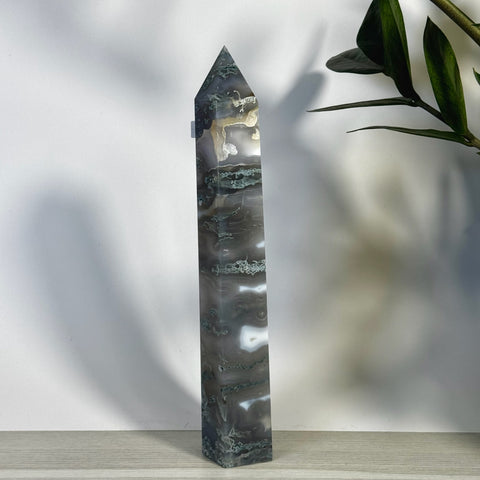 Tall, polished moss agate tower with intricate grey, white, and green patterns, standing on a light wooden surface.