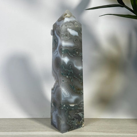 Tall, polished moss agate tower with swirling grey, white, and green patterns, featuring natural raw inclusions.