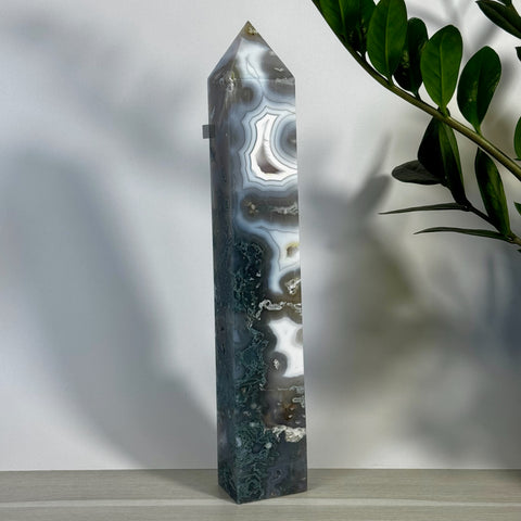 Tall, polished moss agate tower with green, white, and brown swirling patterns, standing next to a green plant.