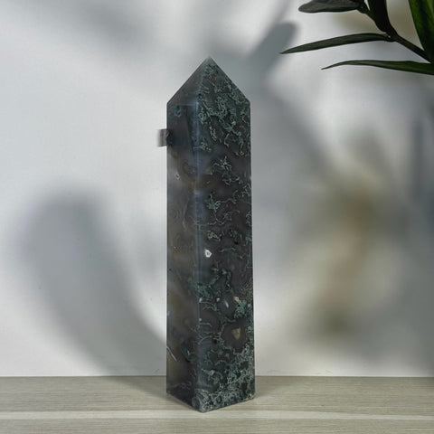 Tall, polished moss agate tower with dark green and white patterns, pointed top, on a light wooden surface.