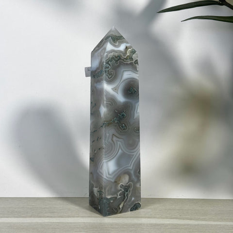 Tall, polished moss agate tower with white, gray, and green swirling patterns, on a light wooden surface.
