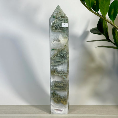 Tall, polished moss agate tower (variant F) with green and white natural patterns, standing on a light wooden surface.