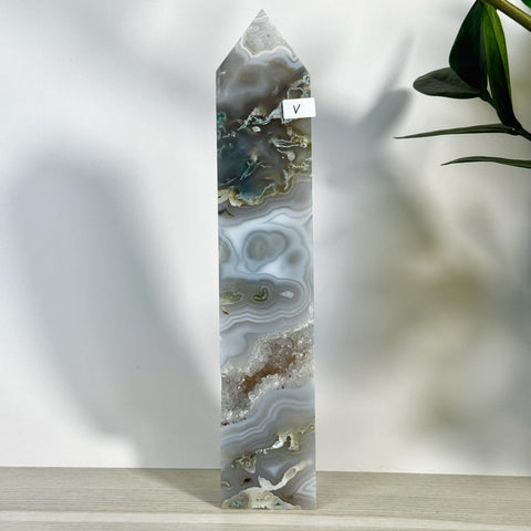 Tall, polished moss agate tower with grey, white, and green bands, featuring a raw crystal geode cavity.