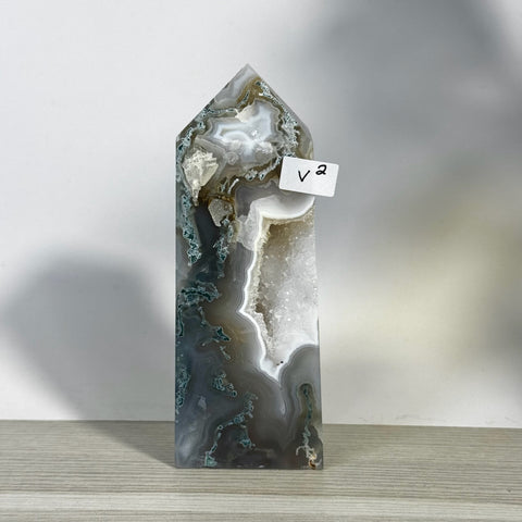 Tall, polished moss agate tower (V2) with grey, white, and green patterns, featuring a sparkling geode cavity.