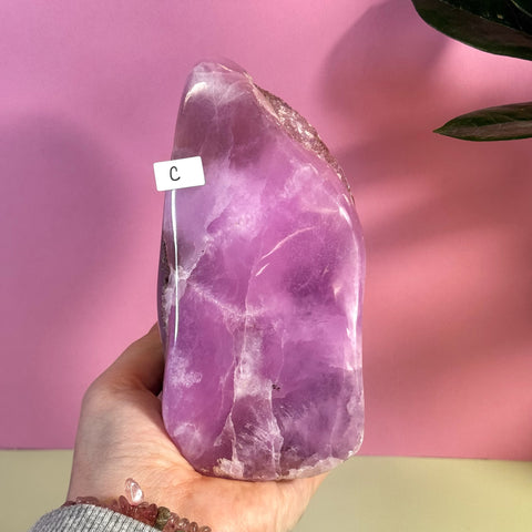 Hand holding a large, polished pink aragonite free form crystal with natural rough edges.