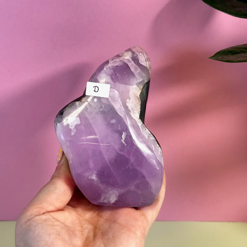 Hand holding a large, free-form pink aragonite crystal with purple hues and white inclusions.