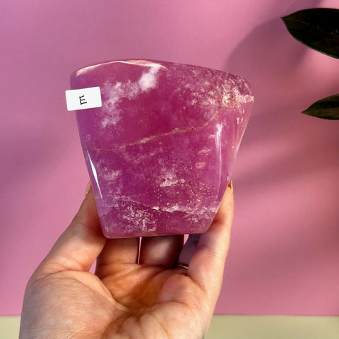 Hand holding a vibrant pink aragonite free form crystal with white inclusions, variant E.