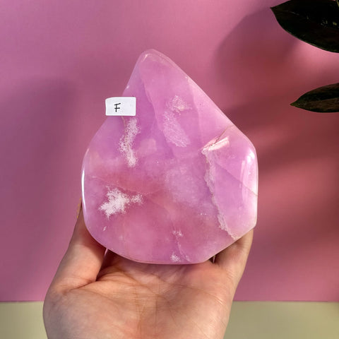 Hand holding a large, polished pink aragonite free form crystal with white inclusions.