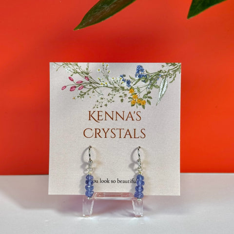 Silver hook earrings with stacked tanzanite beads and clear crystal drops on a floral card.