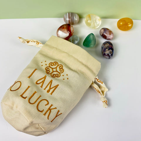 Cream cotton-linen drawstring pouch with gold I AM SO LUCKY embroidery and assorted tumbled crystals.