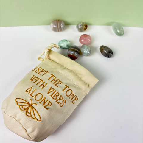Cream cotton-linen drawstring pouch with gold embroidery and moth design, surrounded by assorted polished crystals.