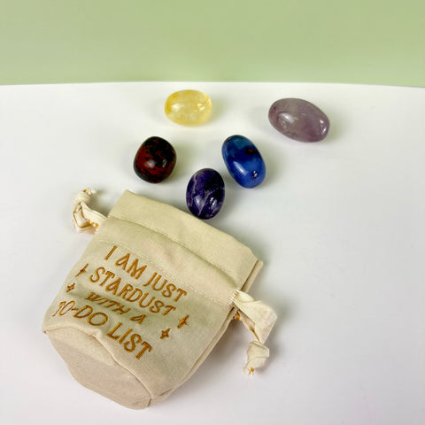Small beige cotton-linen drawstring pouch with gold embroidery and five assorted polished crystals.