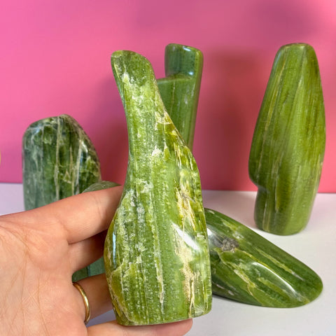 Hand holding a vibrant green tremolite free form crystal with white striations, against a pink background.