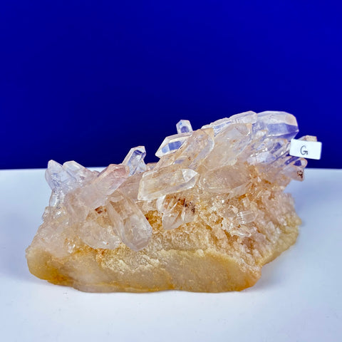 Underworld Himalayan quartz cluster with clear, pointed crystals on a textured, golden-orange mineral base.