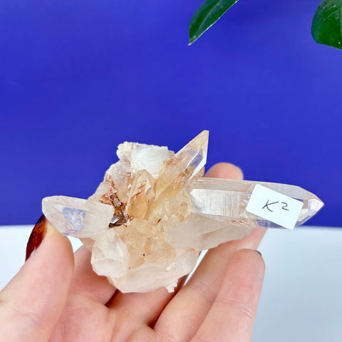 Handheld Himalayan quartz cluster with clear, golden-tinted points and a small K2 identification label.