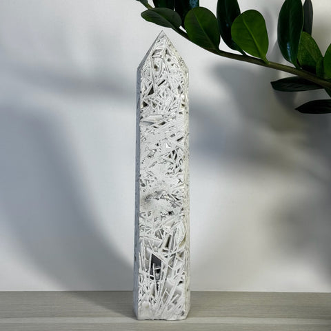 White Lace Agate Tower with intricate web-like patterns, standing tall against a white background with green leaves.
