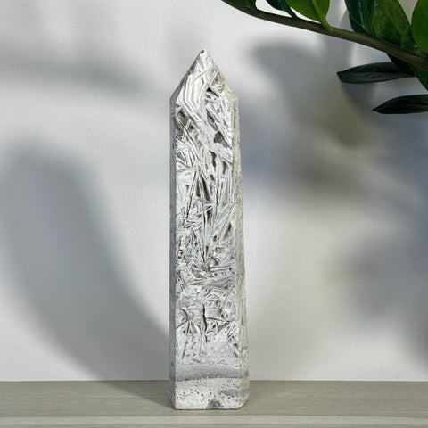 White Lace Agate Tower with intricate, icy patterns and a pointed top, standing on a light wooden surface.