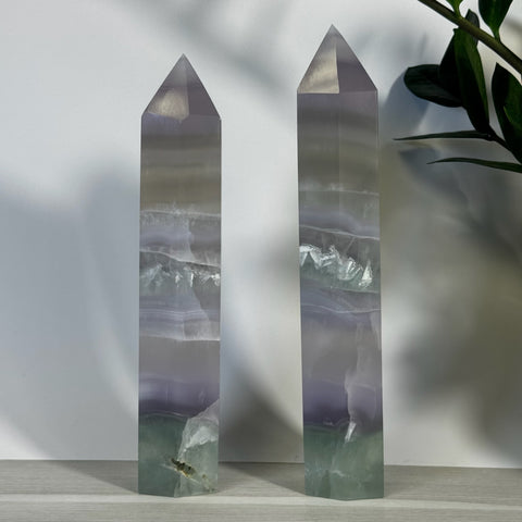 Two tall, polished XL Yttrium Fluorite Towers with purple, white, and green bands.